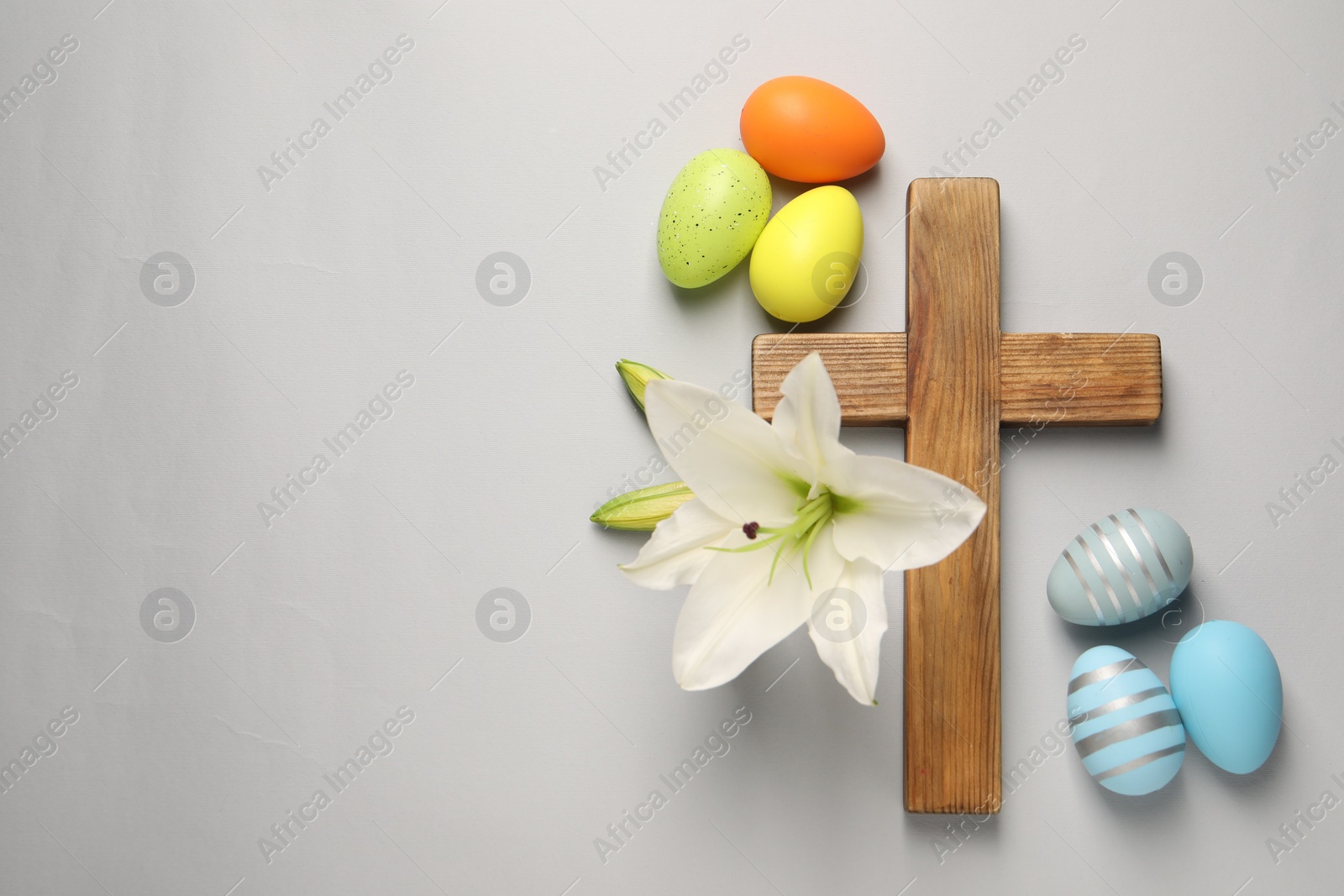 Photo of Wooden cross, painted Easter eggs and lily flowers on grey background, flat lay. Space for text