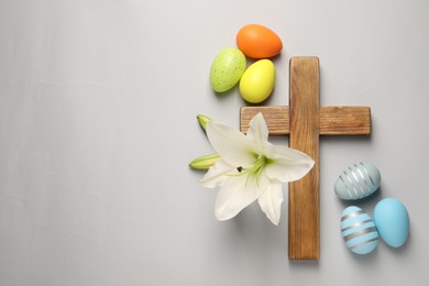 Wooden cross, painted Easter eggs and lily flowers on grey background, flat lay. Space for text