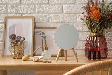 Photo of Mirror, jewelry, makeup products and perfume on wooden dressing table in room