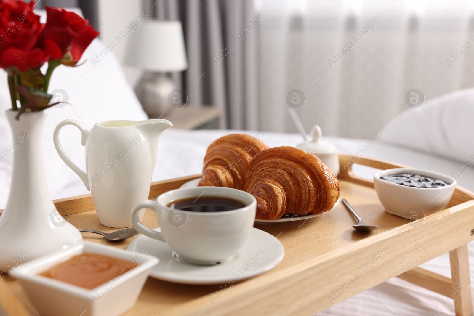 Tasty breakfast served in bed. Fresh croissants, coffee, jam and honey on wooden tray, closeup Photo of Tasty breakfast served in bed. Fresh croissants, coffee, jam and honey on wooden tray, closeup