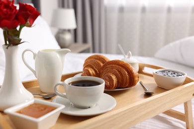 Photo of Tasty breakfast served in bed. Fresh croissants, coffee, jam and honey on wooden tray, closeup