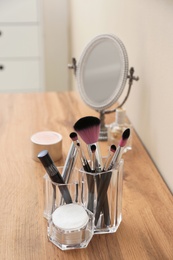 Photo of Organizer with cosmetic products for makeup and mirror on table against light wall