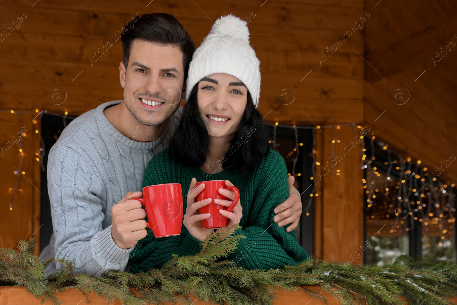 Photo of Happy couple in sweaters with cups near decorated railing