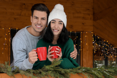 Happy couple in sweaters with cups near decorated railing