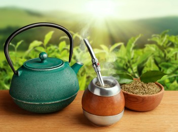 Calabash with mate tea, bombilla and teapot on wooden table outdoors