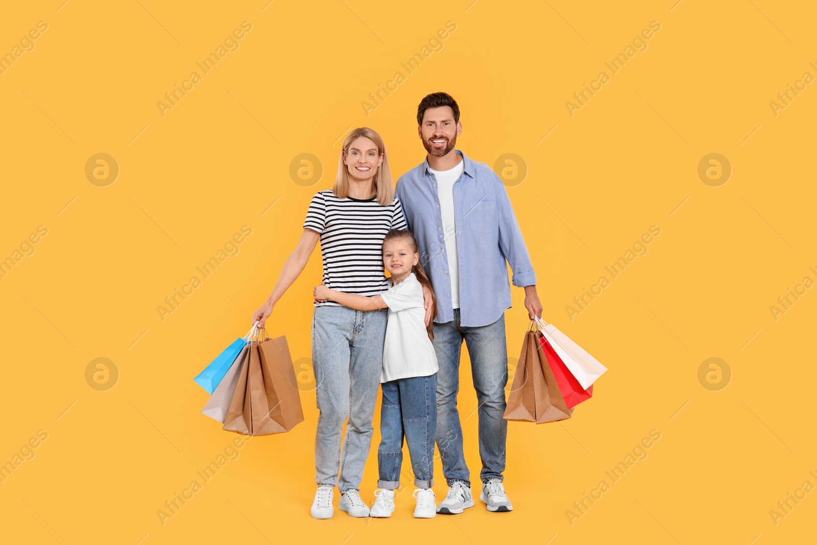 Photo of Family shopping. Happy parents and daughter with paper bags on orange background