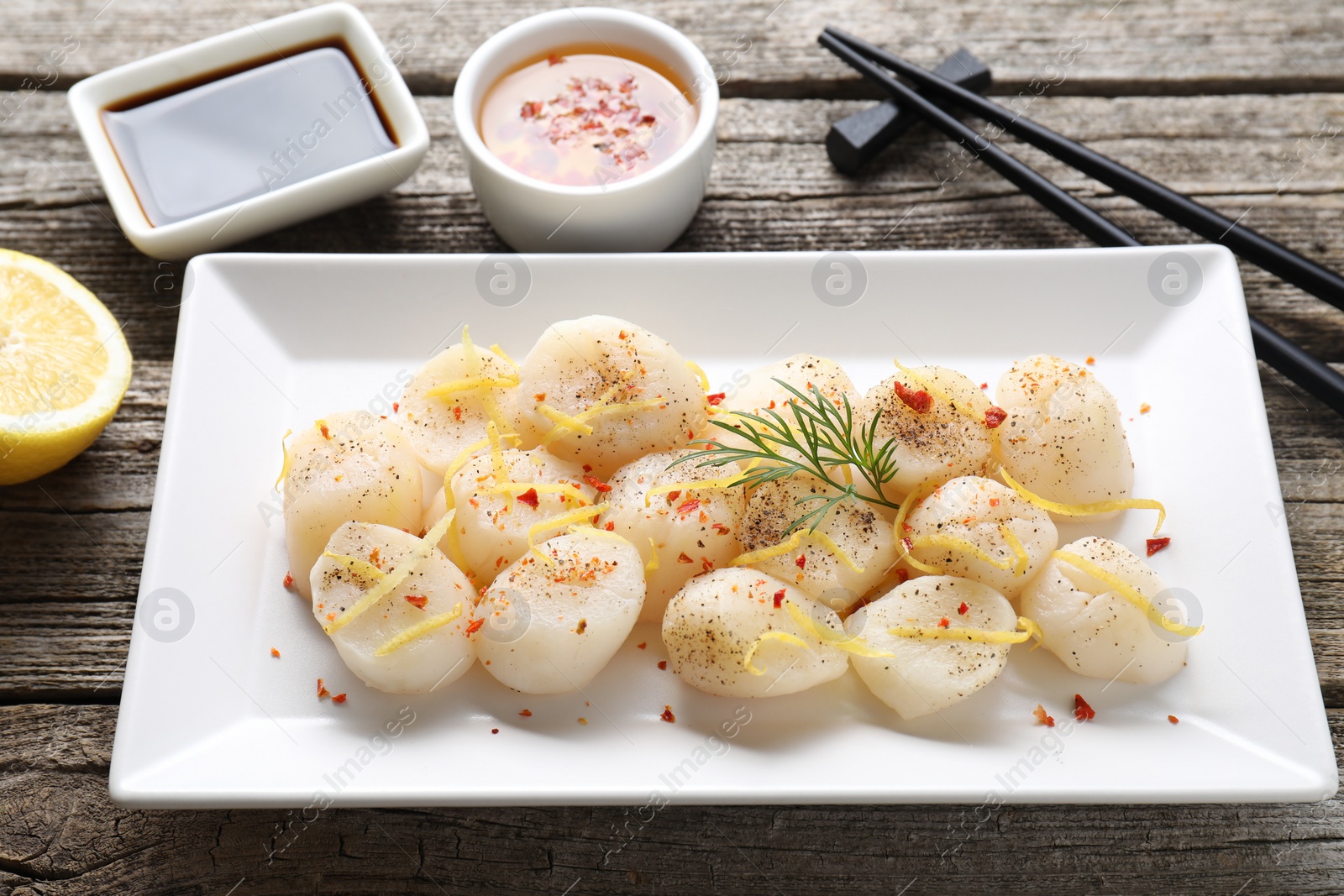 Photo of Raw scallops with spices, dill and lemon zest on wooden table, closeup