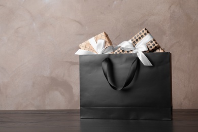 Photo of Paper shopping bag with handles full of gift boxes on table. Mock up for design