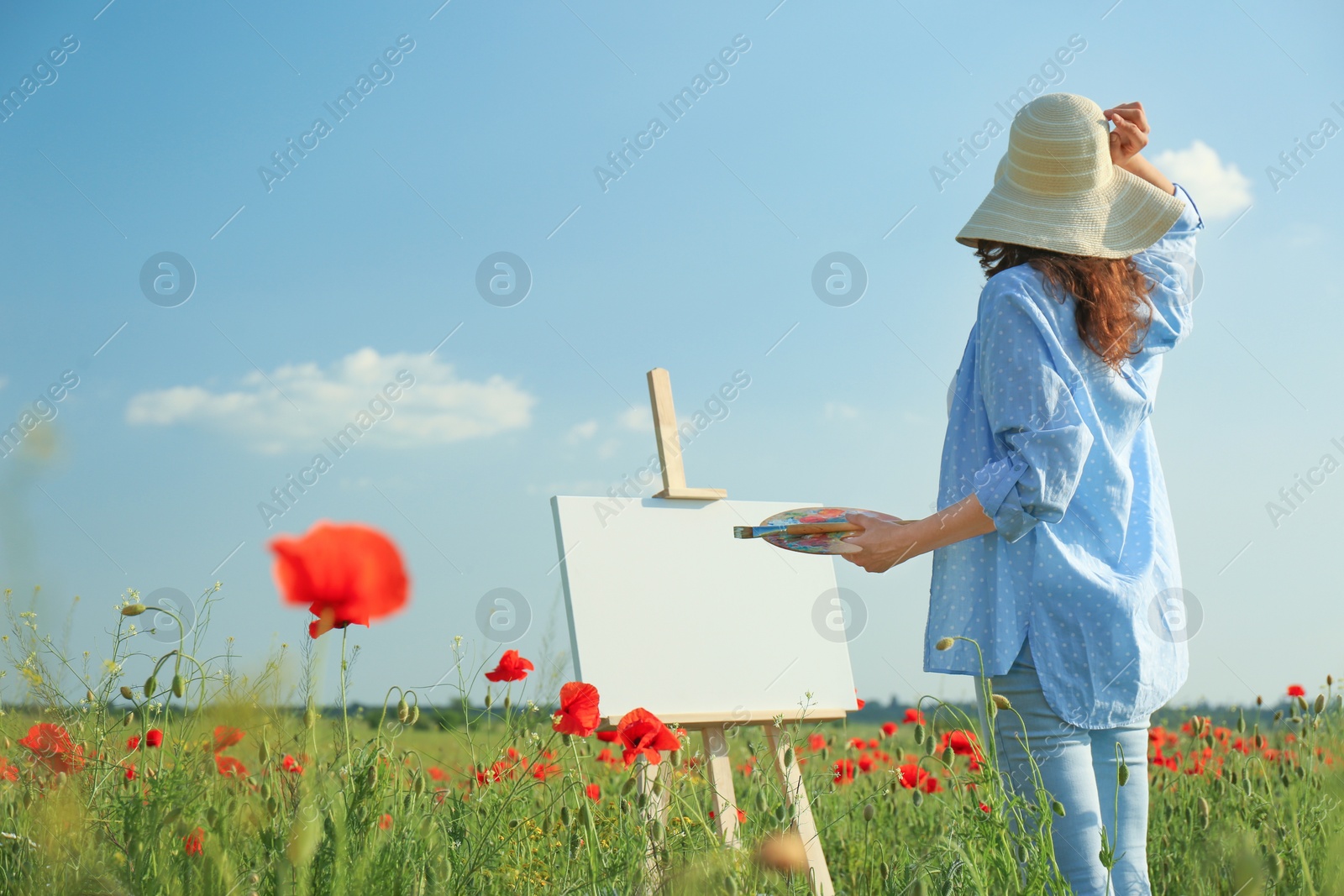 Photo of Woman painting on easel in beautiful poppy field