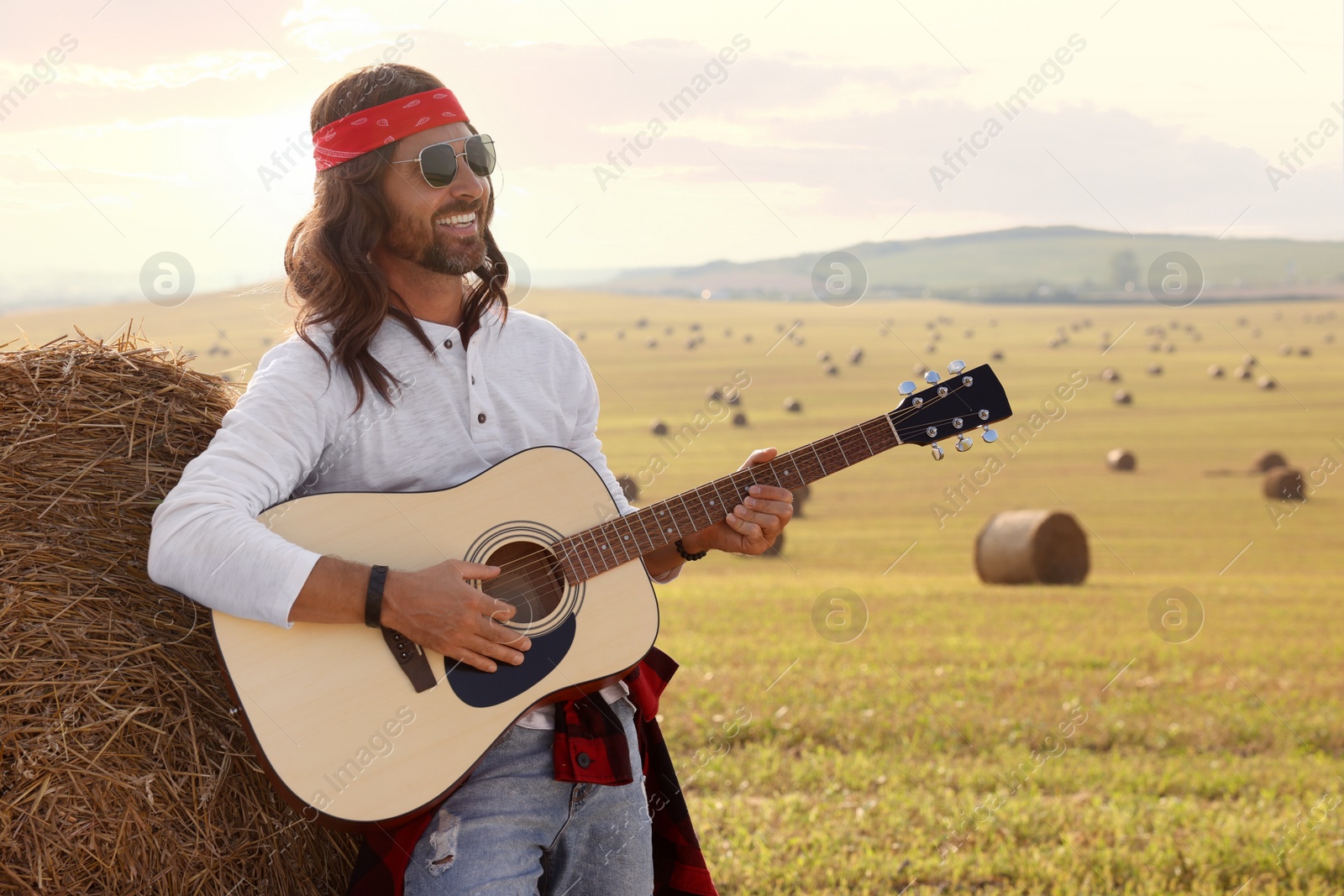 Photo of Hippie man playing guitar near hay bale in field