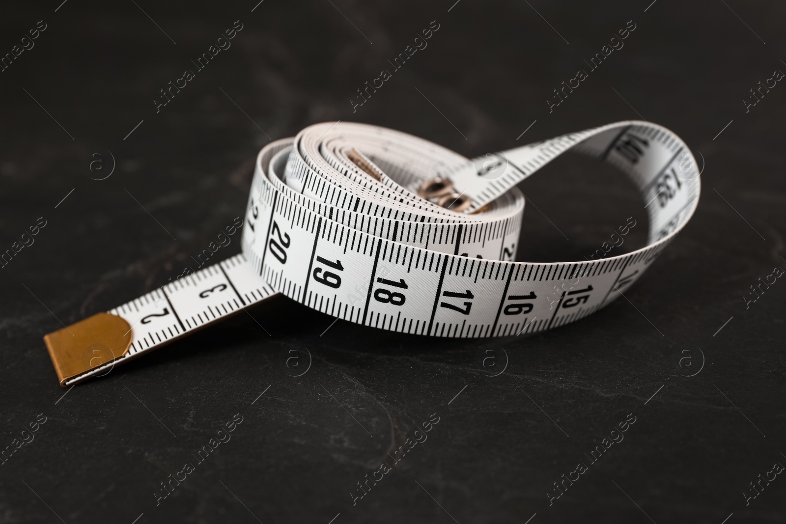 Photo of White measuring tape on black slate table, closeup