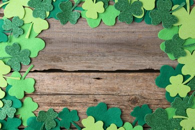 Photo of St. Patrick's day. Frame of decorative clover leaves on wooden background, top view. Space for text