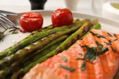 Tasty grilled salmon with tomatoes, asparagus and spices on table, closeup