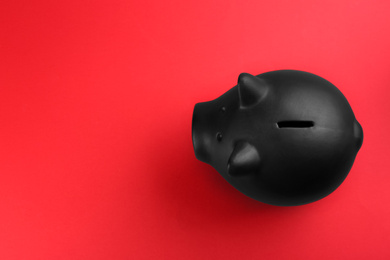 Black piggy bank on red background, top view. Space for text