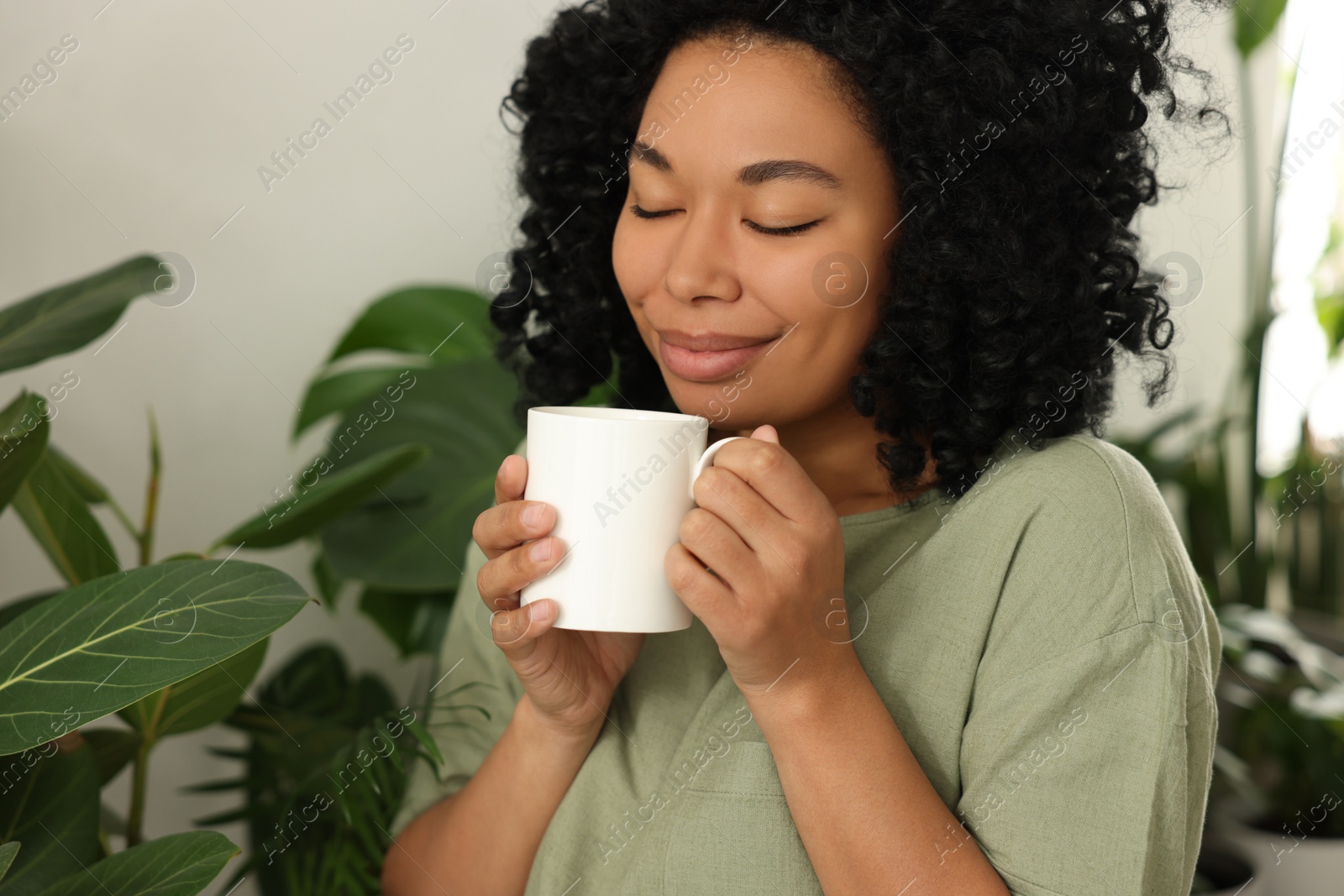 Photo of Relaxing atmosphere. Happy woman with cup of hot drink near beautiful houseplants