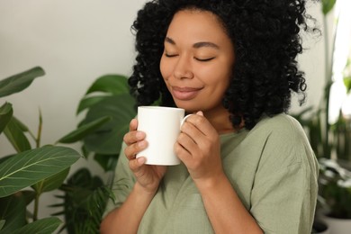 Relaxing atmosphere. Happy woman with cup of hot drink near beautiful houseplants