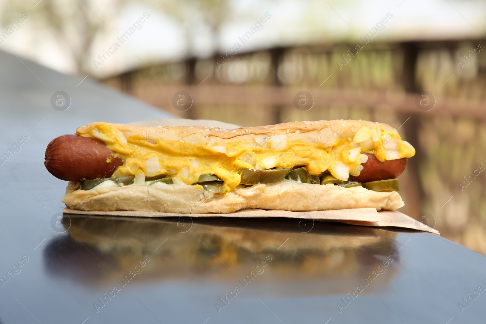 Photo of Fresh tasty hot dog with sauce on dark parapet outdoors