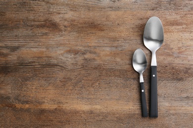 Clean empty table spoons on wooden background, top view. Space for text