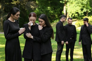 Photo of Sad people in black clothes mourning outdoors. Funeral ceremony
