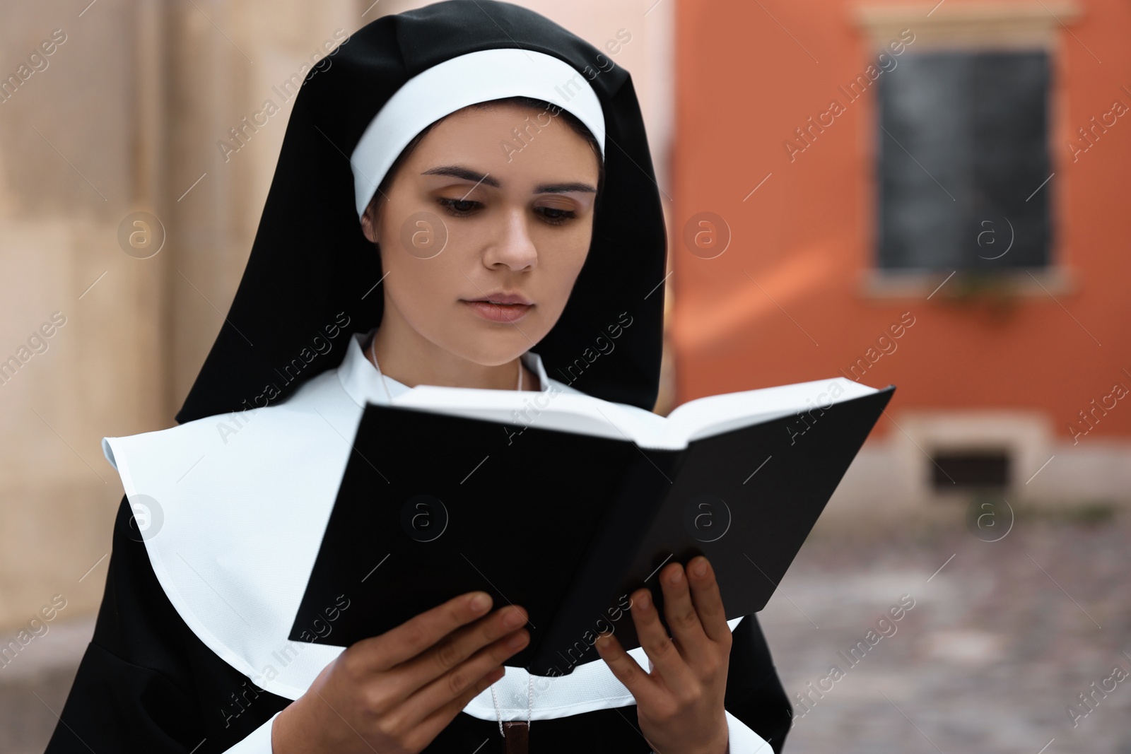 Photo of Young nun reading Bible near building outdoors