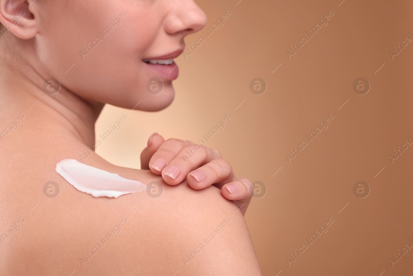 Photo of Woman with smear of body cream on her shoulder against light brown background, closeup. Space for text