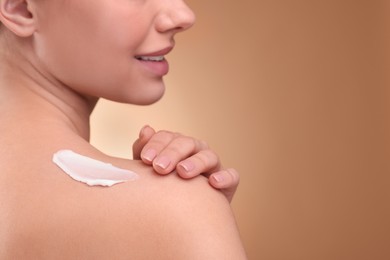 Woman with smear of body cream on her shoulder against light brown background, closeup. Space for text