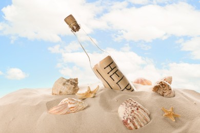 Photo of Corked glass bottle with Help note and seashells on sand against sky