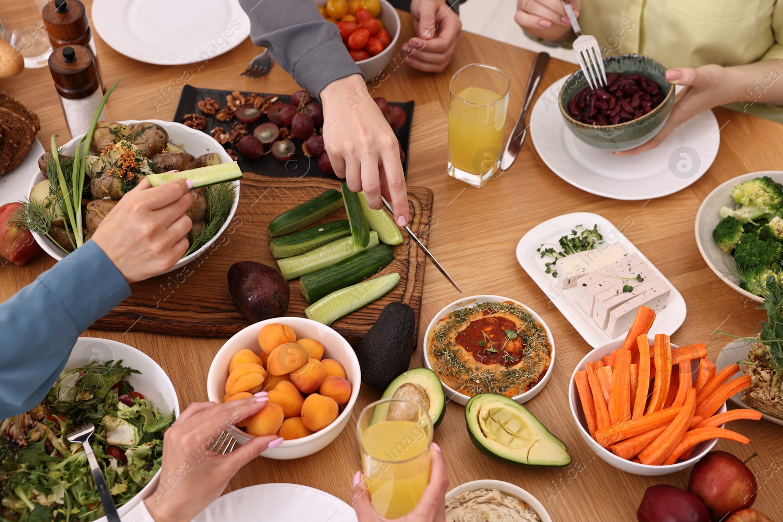 Photo of Friends eating vegetarian food at wooden table indoors, closeup