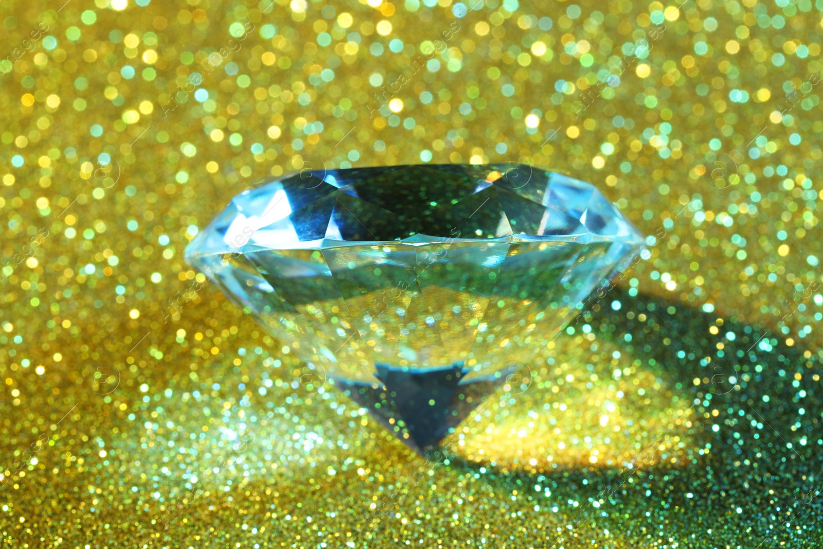 Photo of Beautiful dazzling diamond on glitter background, closeup