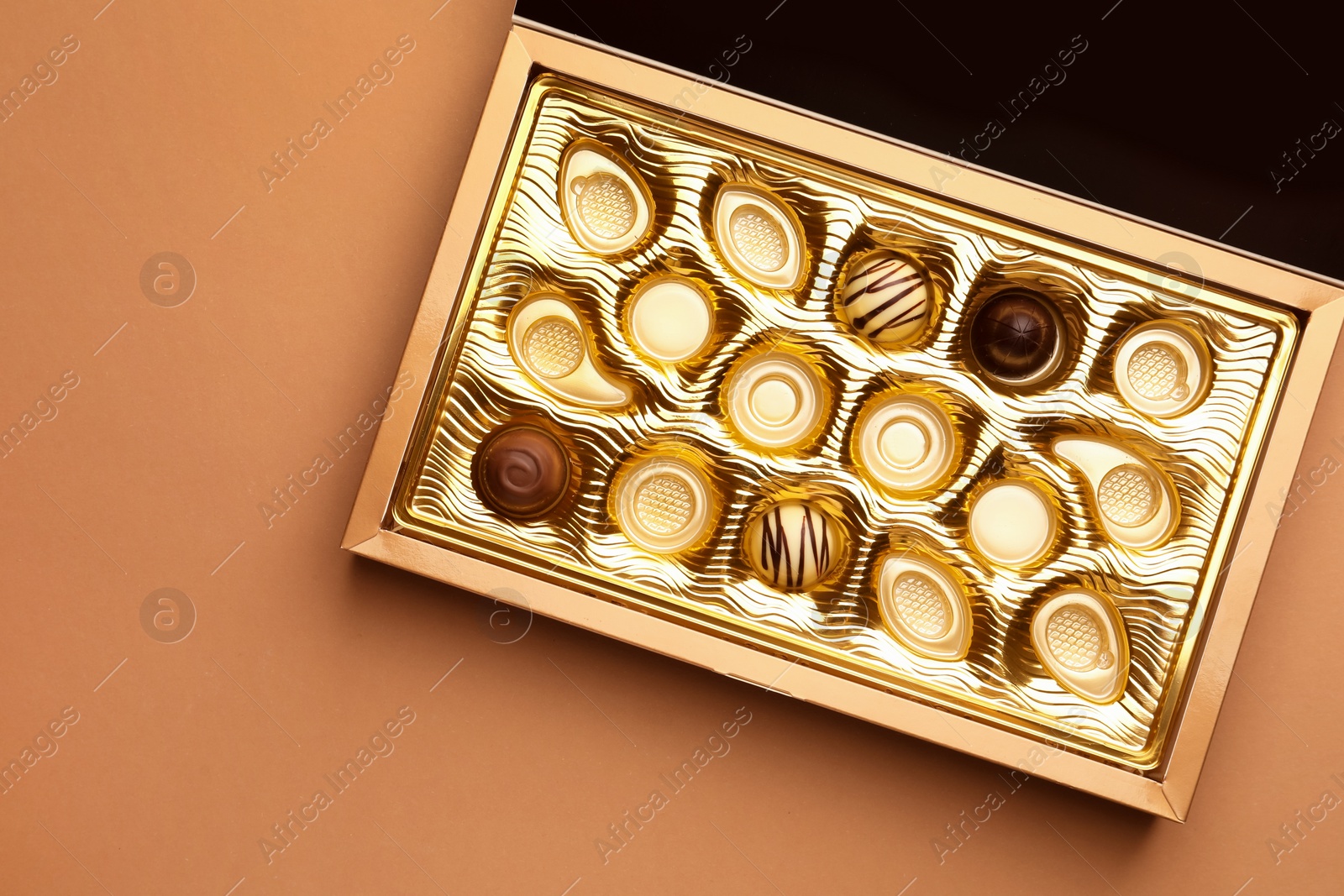 Photo of Partially empty box of chocolate candies on light brown background, top view. Space for text