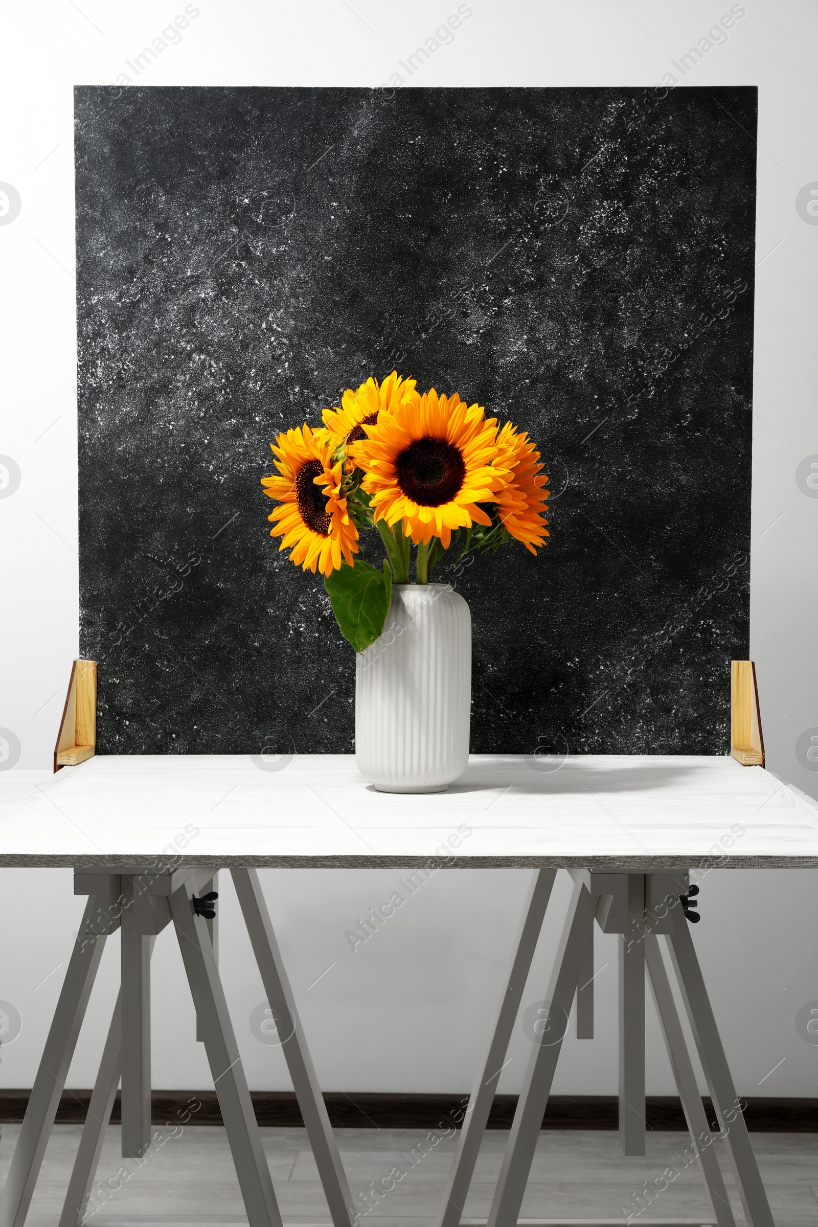 Photo of Vase with beautiful sunflowers and double-sided backdrop on table in photo studio