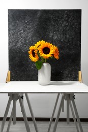 Vase with beautiful sunflowers and double-sided backdrop on table in photo studio