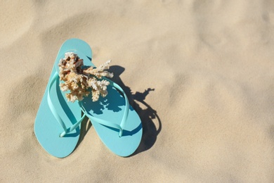 Photo of Stylish flip flops and beautiful coral on sand near sea, top view. Beach accessories for summer vacation