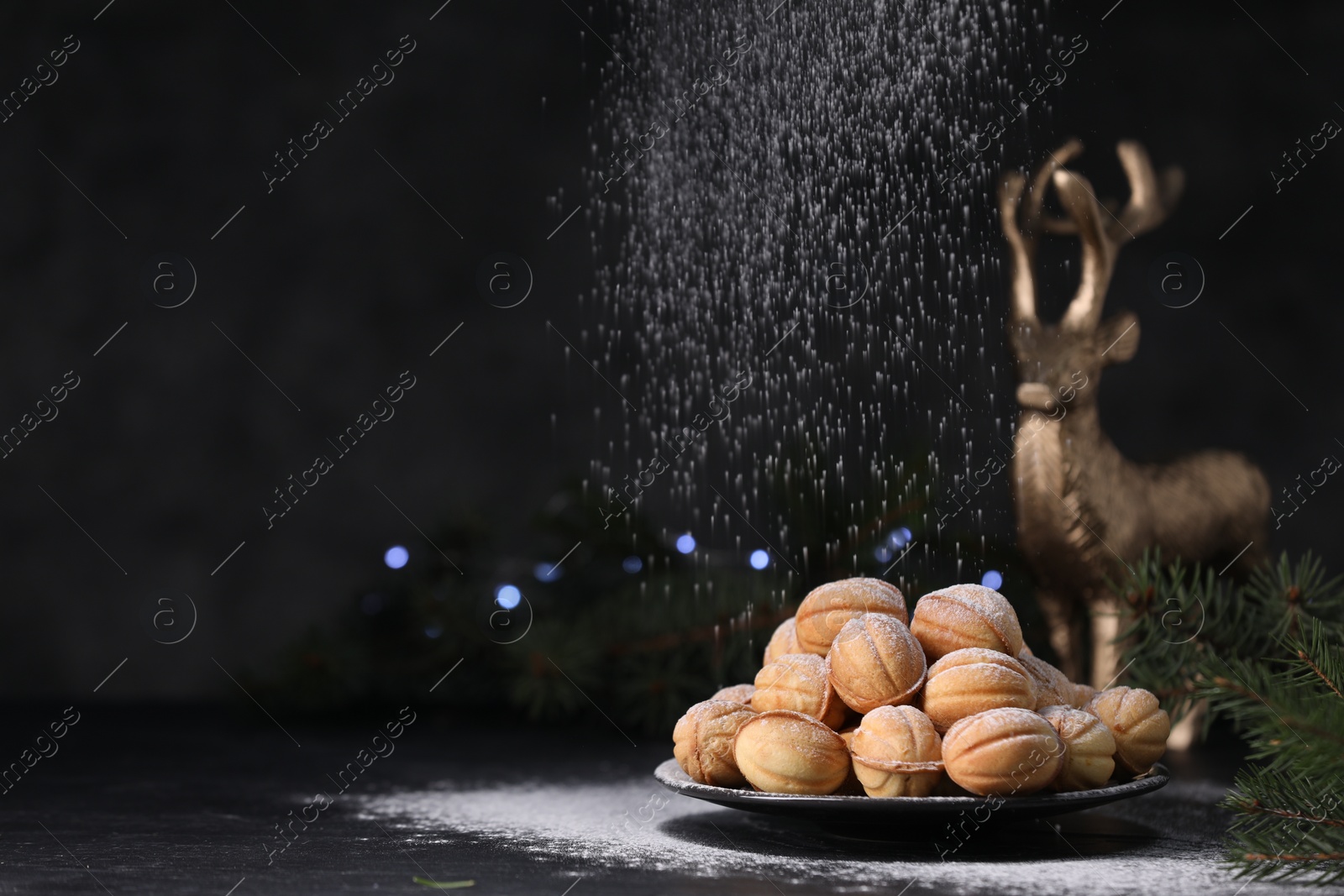 Photo of Adding powdered sugar onto tasty nut shaped cookies on black table. Space for text