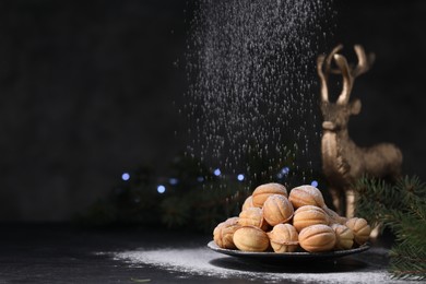 Photo of Adding powdered sugar onto tasty nut shaped cookies on black table. Space for text