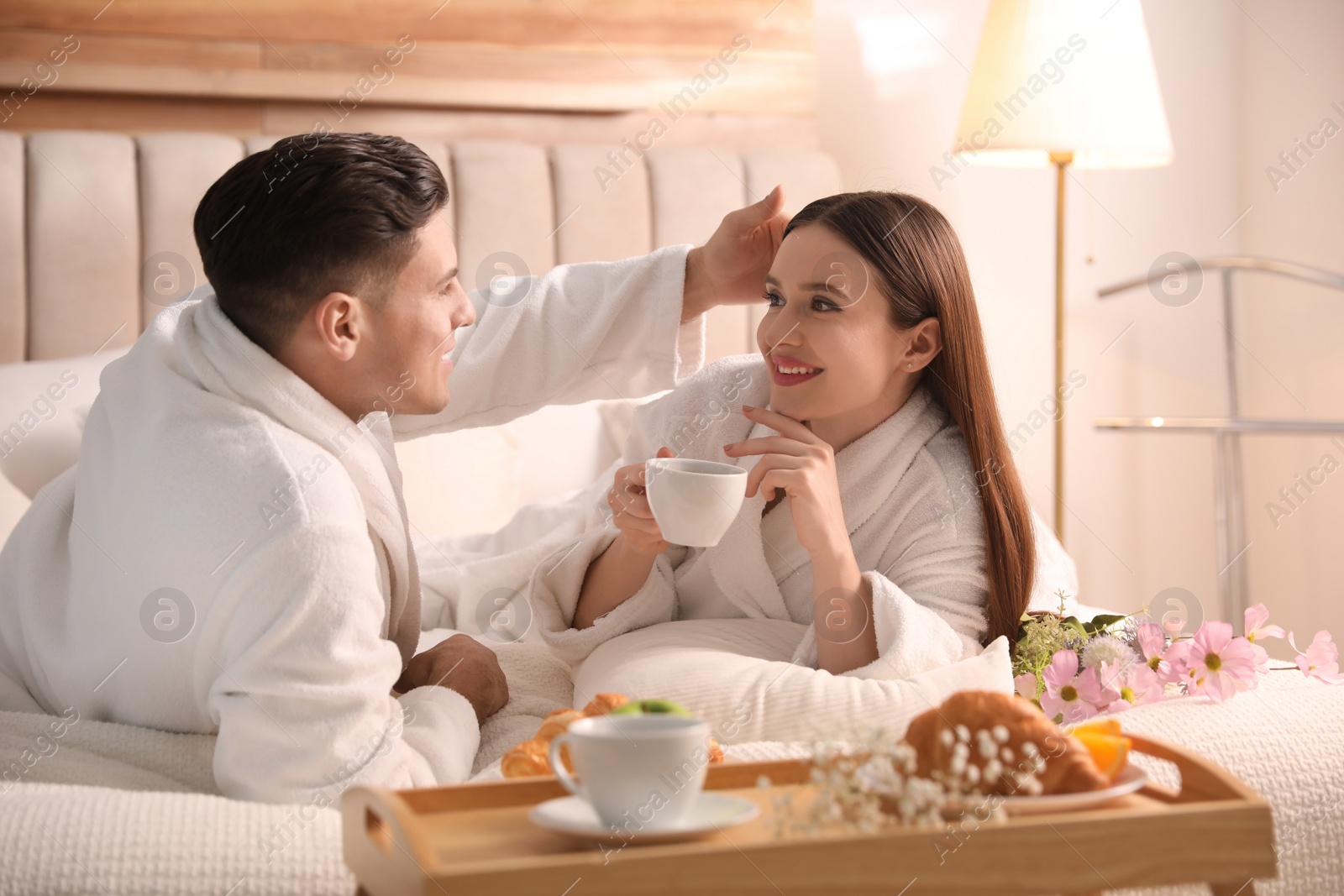 Photo of Happy couple in bathrobes having breakfast on bed at home