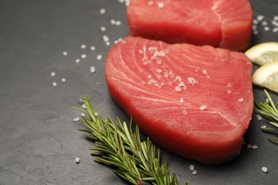 Photo of Raw tuna fillets with rosemary, sea salt and lemon slices on black table, closeup. Space for text