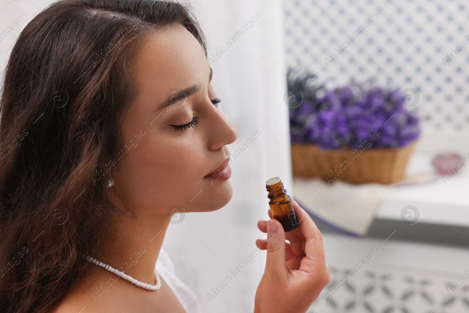 Photo of Beautiful young woman with bottle of essential oil indoors