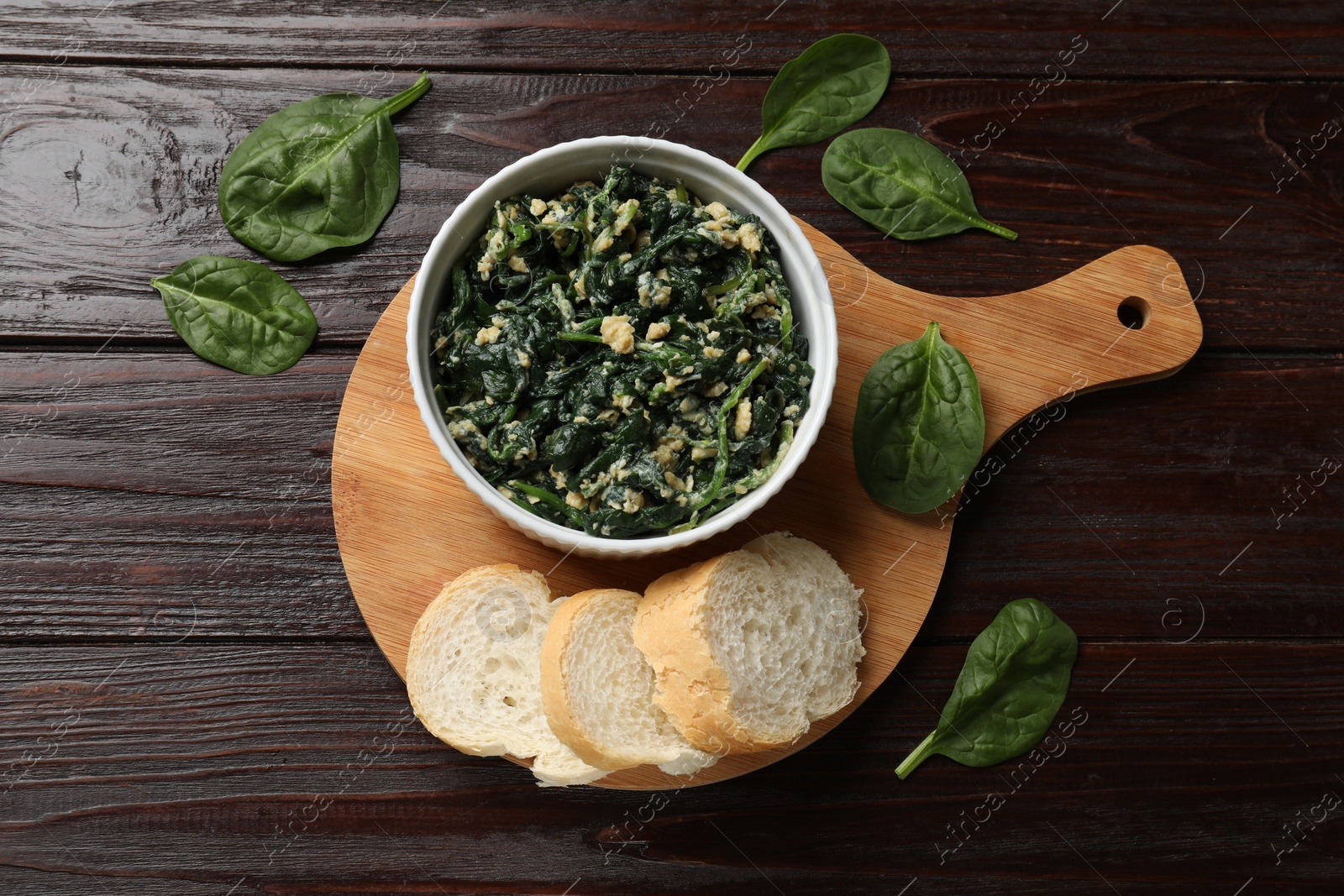 Photo of Tasty spinach dip with egg in bowl and bread on wooden table, top view