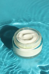 Photo of Jar with moisturizing cream in water on light blue background