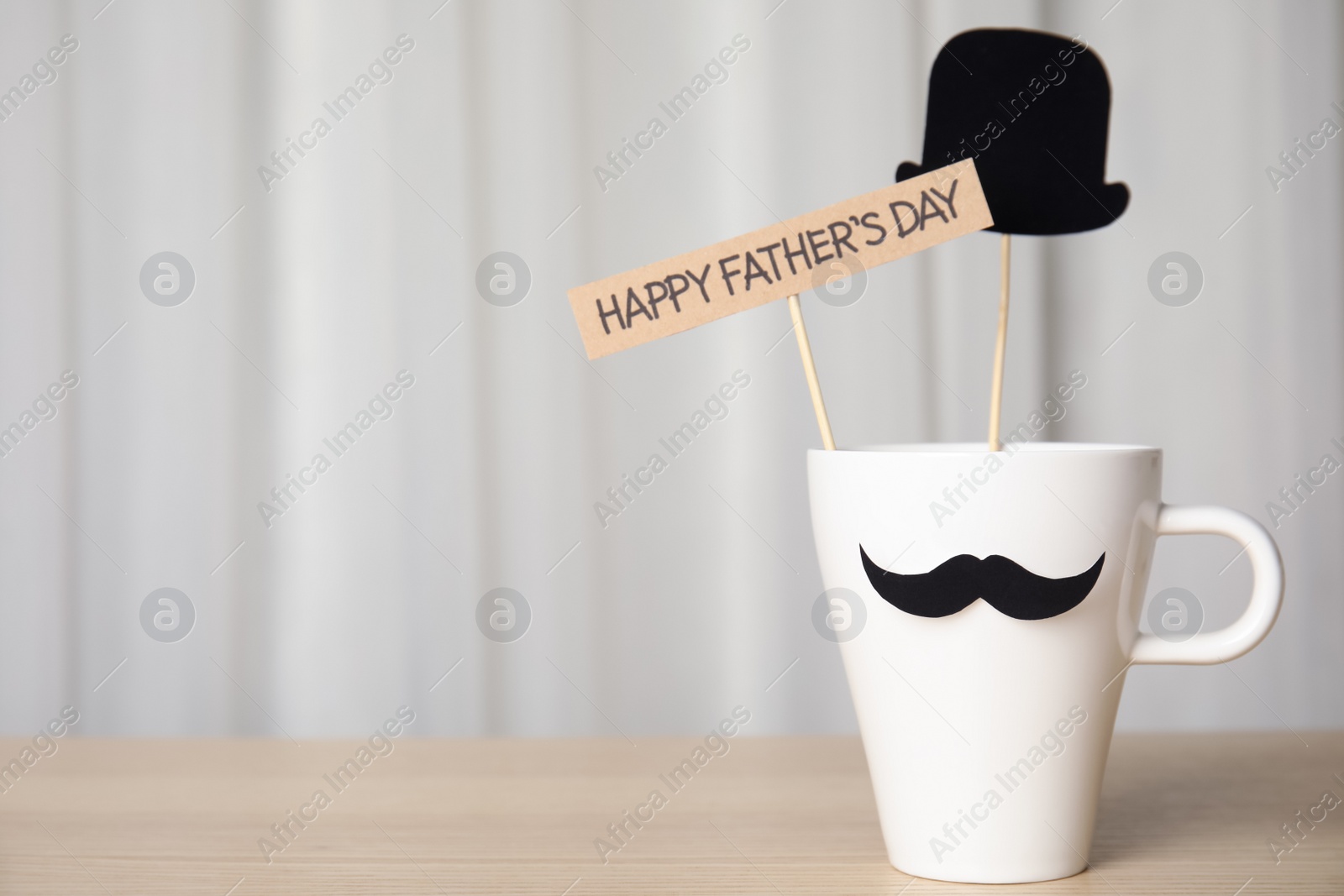 Photo of Cup with paper mustache, hat and sign HAPPY FATHER'S DAY on wooden table, space for text