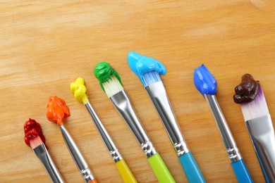 Brushes with colorful paints on wooden background, flat lay