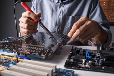 Photo of Technician repairing electronic circuit board with soldering iron at table, closeup