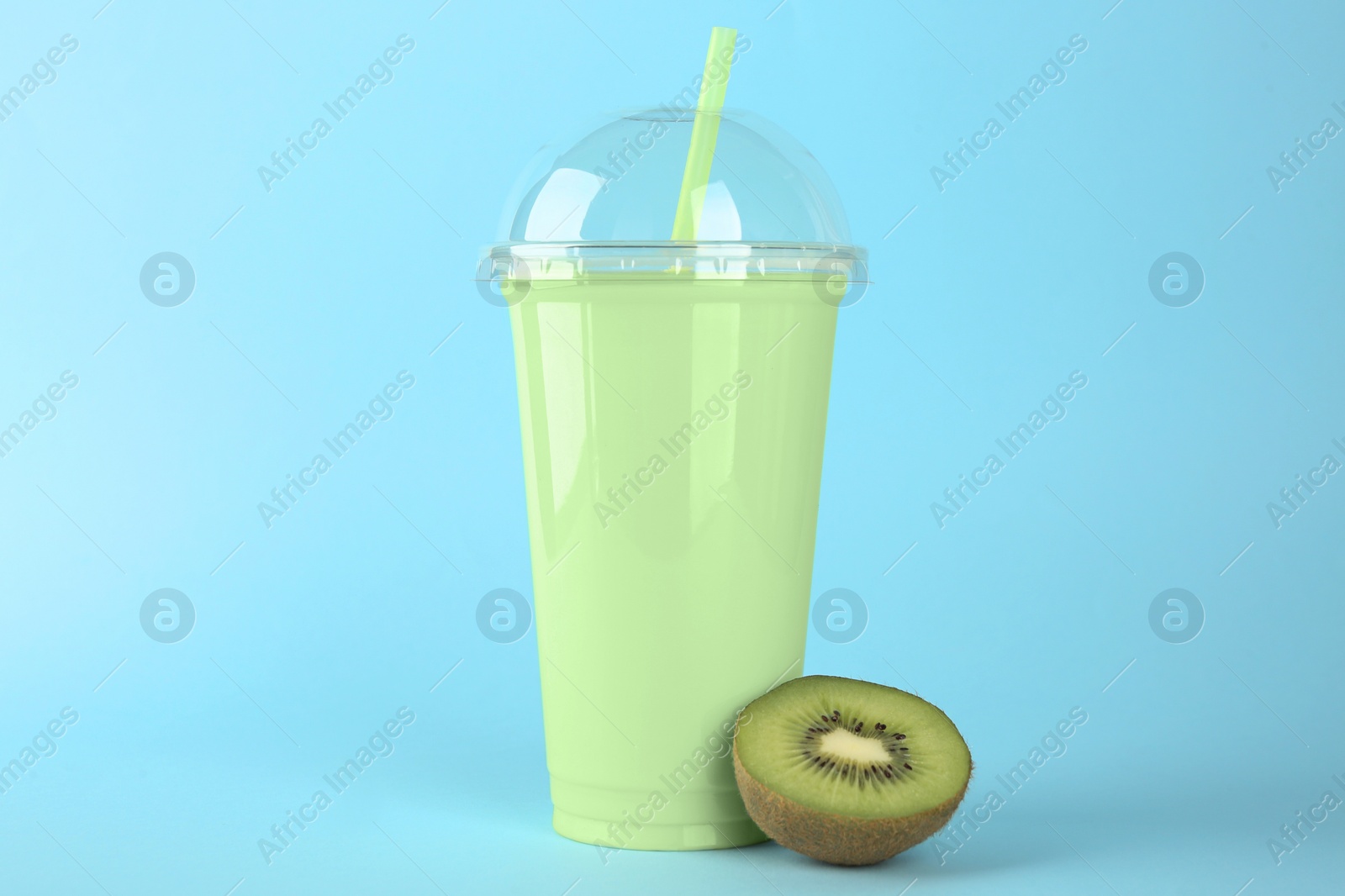 Photo of Plastic cup of tasty smoothie and fresh kiwi on light blue background