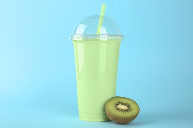 Photo of Plastic cup of tasty smoothie and fresh kiwi on light blue background