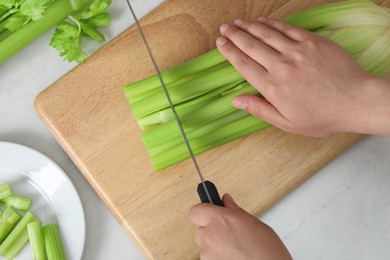 Woman cutting fresh green celery at white table, top view