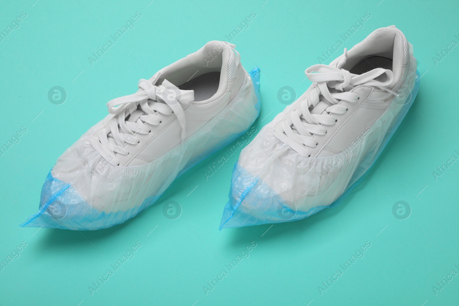 Photo of Sneakers in shoe covers on turquoise background, closeup