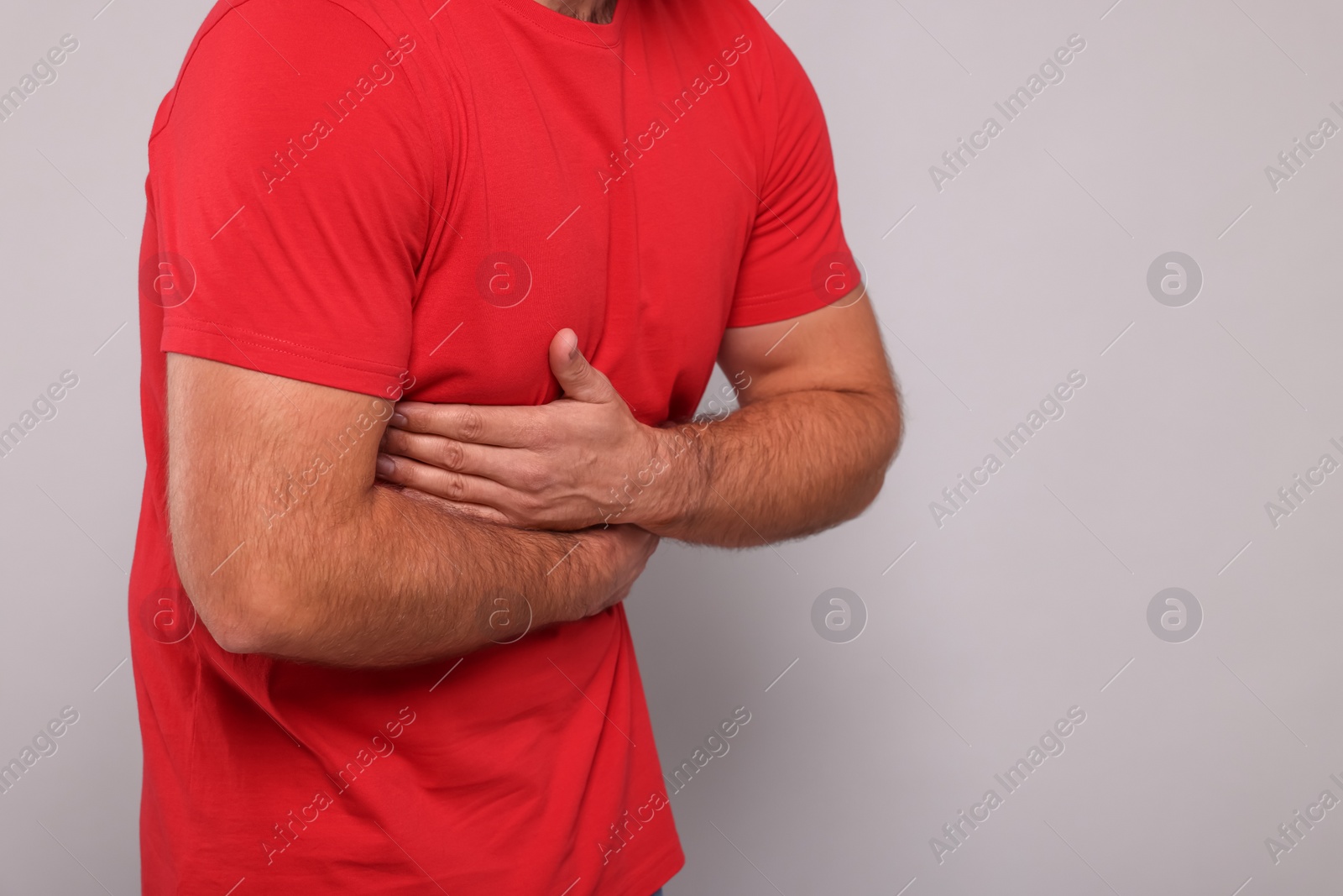 Photo of Man suffering from stomach pain on grey background, closeup. Space for text