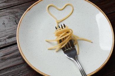 Photo of Heart made of tasty spaghetti and fork on wooden table, closeup