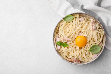 Photo of Bowl of tasty pasta Carbonara with basil leaves and egg yolk on light grey table, top view. Space for text